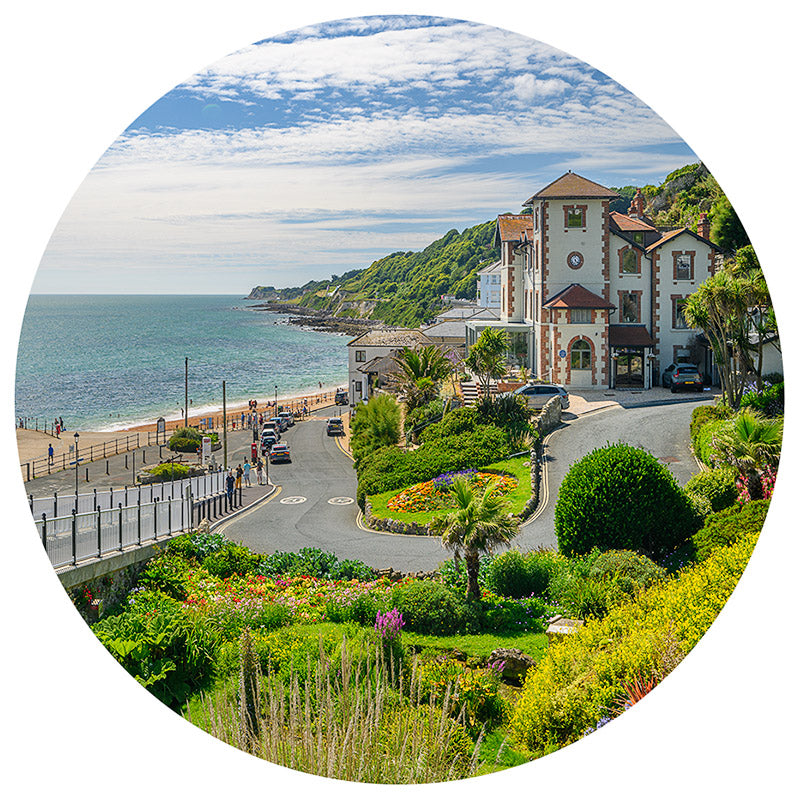 Coastal scene captured in the Ventnor bauble by Available Light Photography, featuring a curving road edged by seaside buildings and lush greenery under a partly cloudy sky.