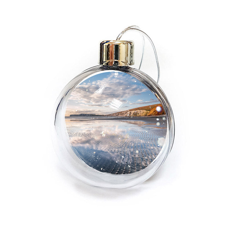 The Compton Bay bauble by Available Light Photography showcases a serene beach scene with calm waves, a cloudy sky, and distant cliffs within its round, transparent design.