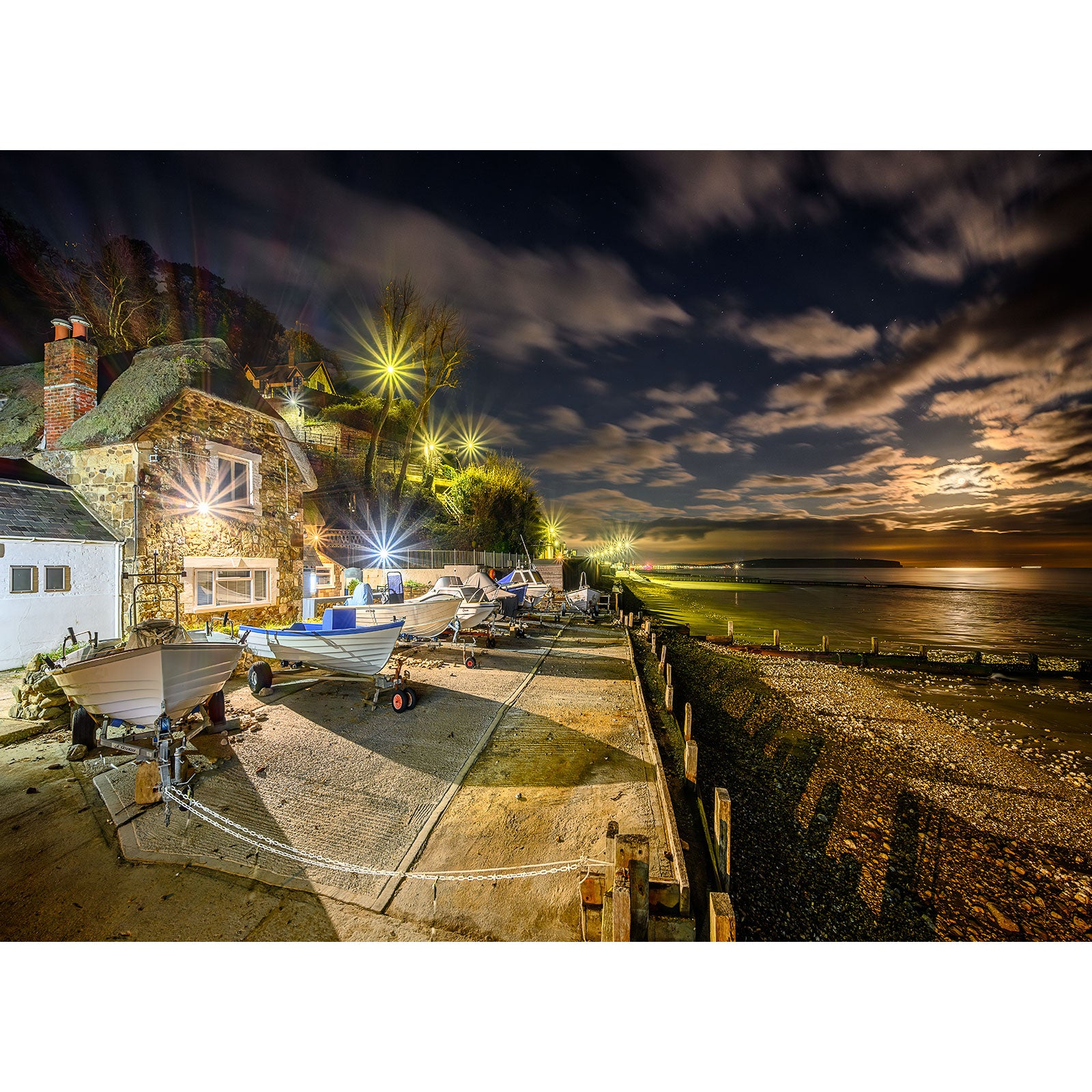 Nighttime at a coastal village with boats parked on a slipway and a Shanklin by Moonlight sky over the Wight by Available Light Photography.