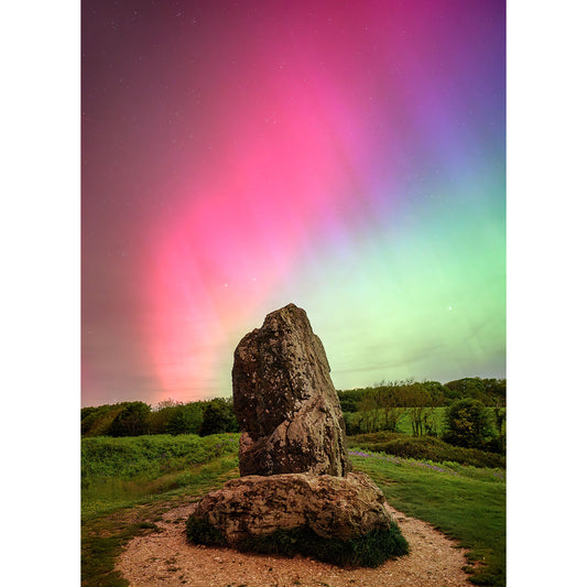 A large standing stone is set in a grassy landscape on the Isle of Wight, under a vibrant night sky with pink and green Northern Lights in "The Northern Lights, The Longstone" by Available Light Photography.