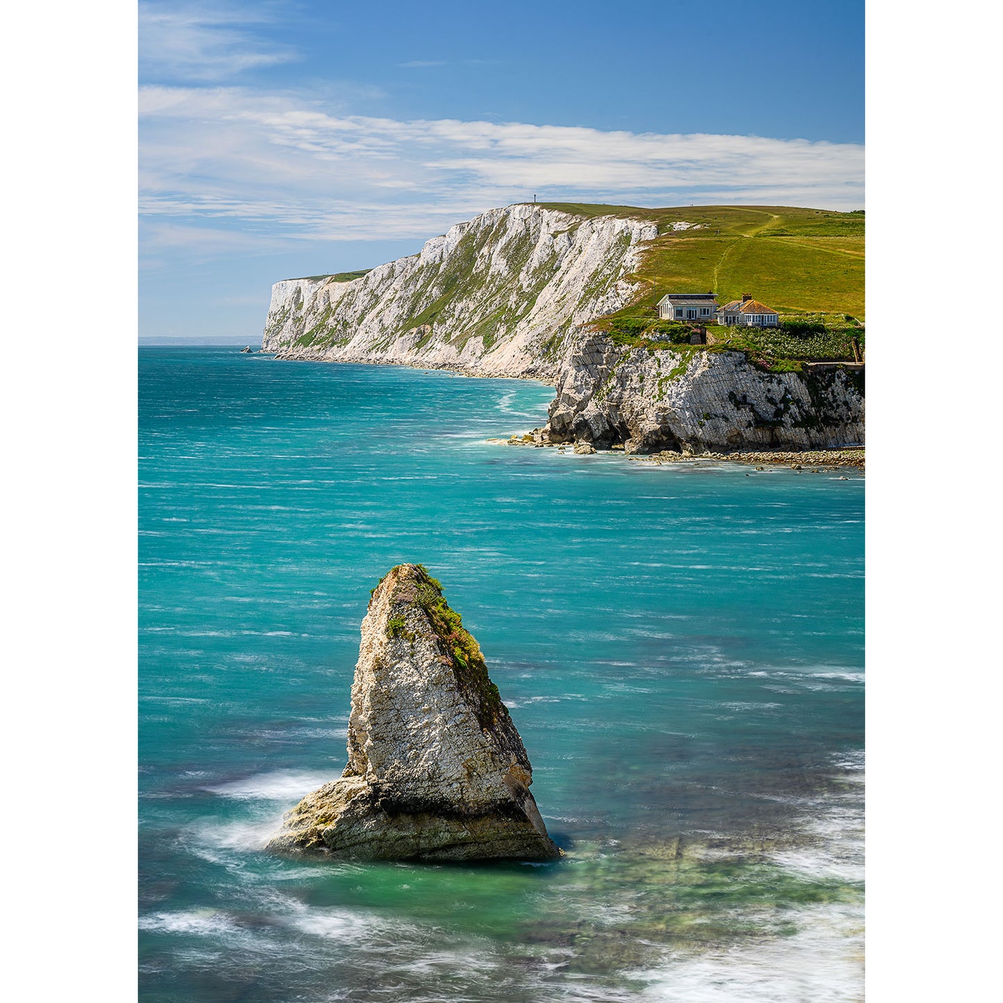 A 1992 image captures a single coastal rock formation standing in turquoise waters, with a white cliff and some small structures on the cliff edge in the background under a partly cloudy sky. This captivating scene is part of the "Freshwater Bay" collection by Available Light Photography.