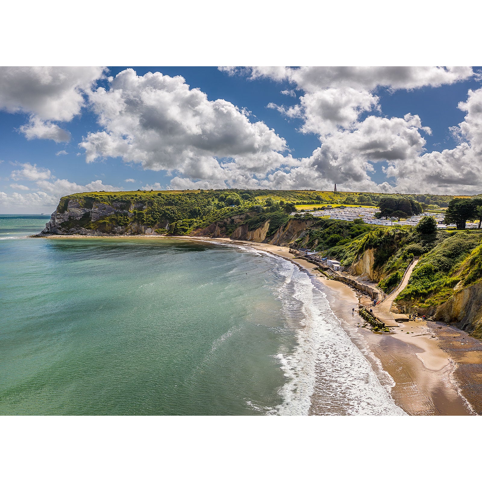 Image number 2885 depicts Whitecliff Bay, a coastal landscape with a sandy beach, cliffs, green hills, and scattered buildings under a partly cloudy sky by Available Light Photography.