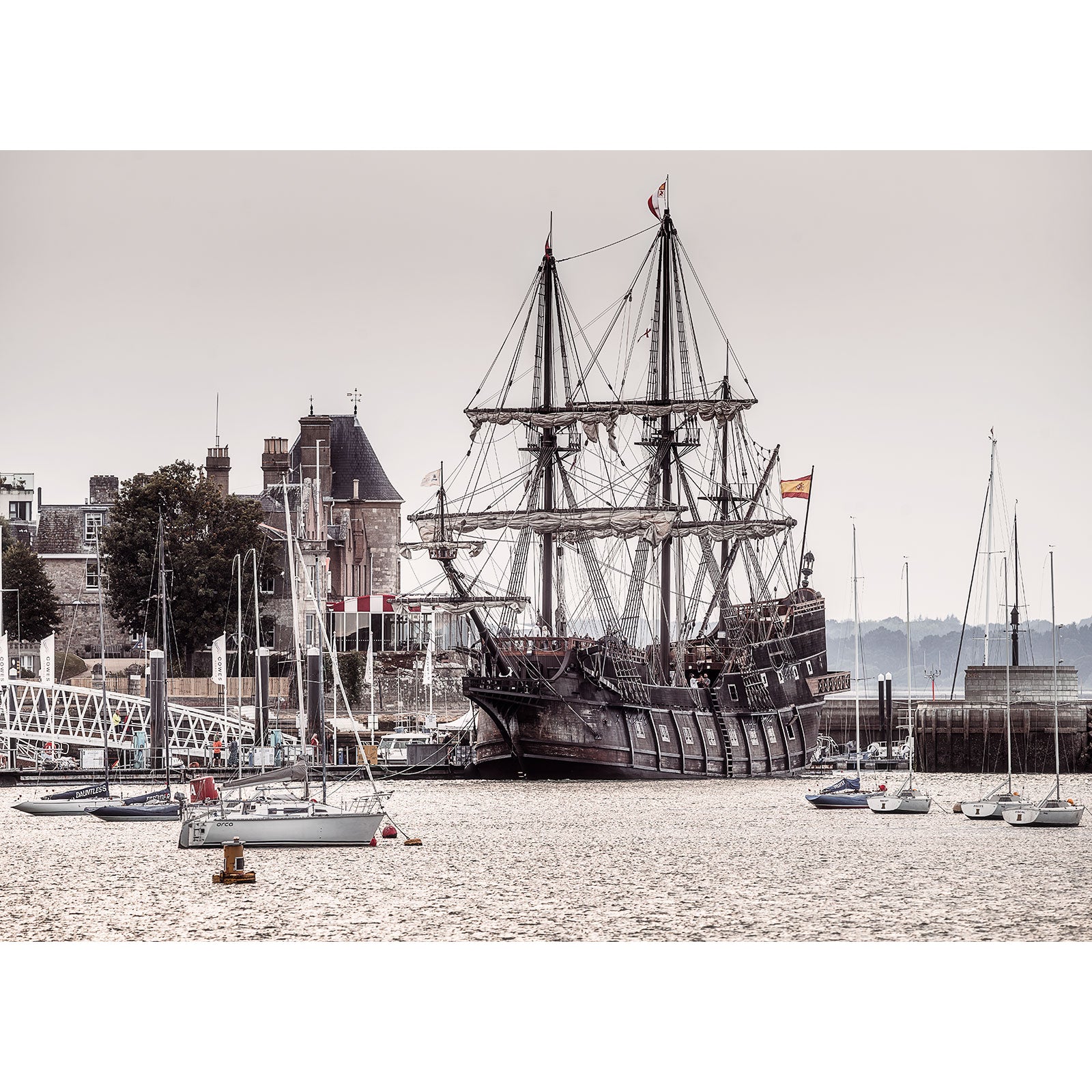 A large sailing ship, El Galeón Andalucía, is docked at a port near several smaller boats with buildings and trees in the background; Image number 2914 by Available Light Photography captures this serene harbor scene.