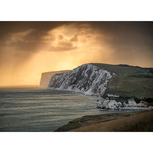 Image number 2770, titled "Tennyson Down" by Available Light Photography, captures a dramatic sky with a golden sunset illuminating white chalk cliffs along the coastline, with waves crashing against the shore and a small building near the water's edge.