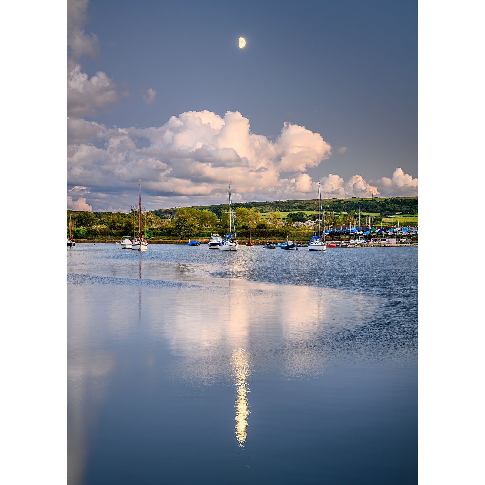 The tranquil lakeside scene of Bembridge Harbour captured by Available Light Photography in image number 2921, features sailboats docked on calm water reflecting the partly cloudy sky with a visible moon above.