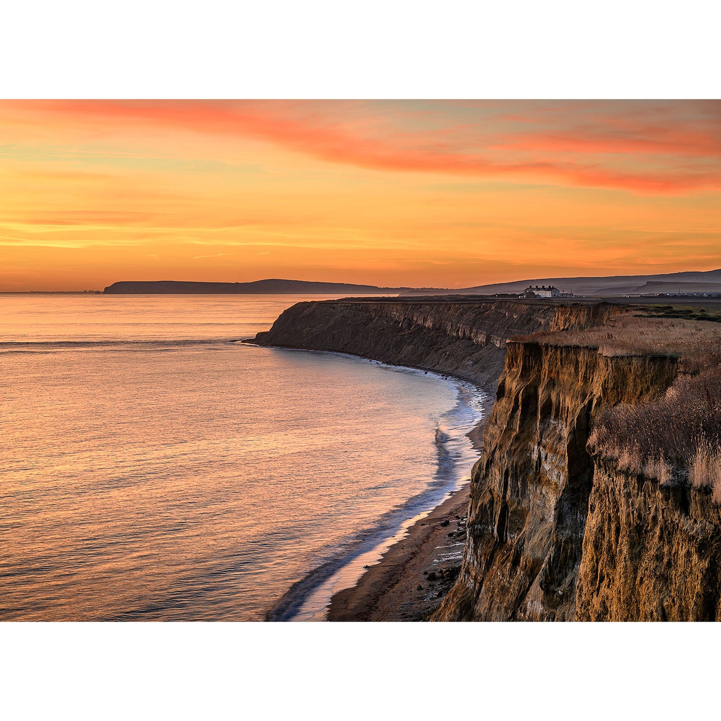 Watching the sunset from the coastal cliffs is breathtaking, as the orange and pink sky beautifully reflects on the tranquil ocean while gentle waves caress the shore—a perfect moment captured by Available Light Photography's "Chale.