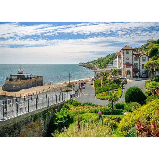 A picturesque coastal view featuring a pier, beach, and vibrant gardens surrounds the pristine white building of "Ventnor" by Available Light Photography. The blue sky dotted with scattered clouds adds to the serene atmosphere. Apologies for any inconvenience; feel free to provide more details for a thorough description.