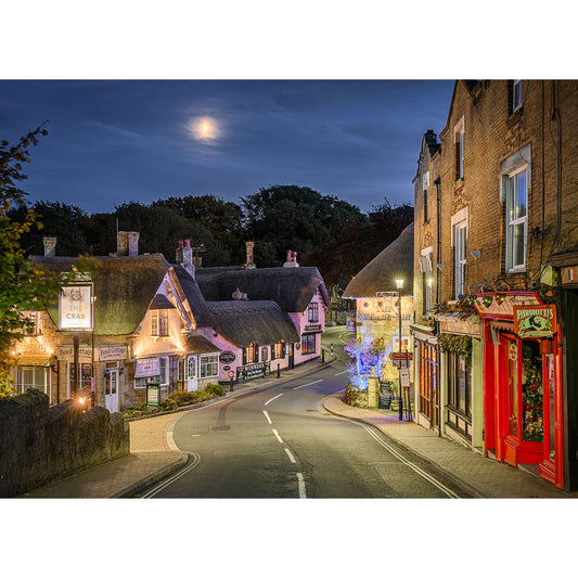 Certainly! Here's a revised version of the description with "Shanklin Old Village" and "Available Light Photography" integrated:

A quaint village street at night, Shanklin Old Village illuminated by shop lights and a full moon. Captured by Available Light Photography, the scene features charming old buildings with thatched roofs and a quiet, winding road.