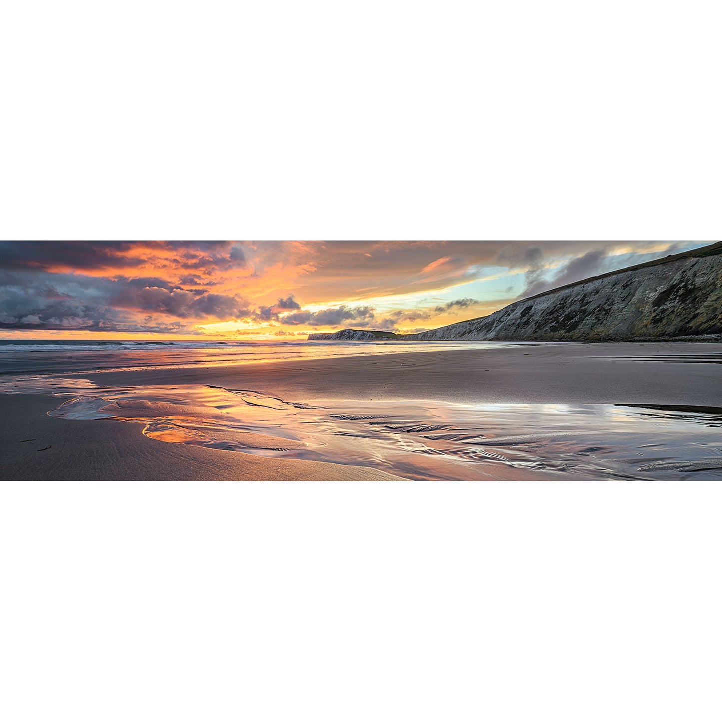 Experience the beauty of Compton Bay, where rolling waves gently caress reflective wet sand against a backdrop of distant cliffs under a cloudy sky. This breathtaking scene is captured by Available Light Photography.