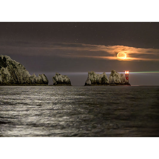 Moonset over The Needles by Available Light Photography captures a serene glow on the rock formation and lighthouse, with a tranquil sea in the foreground.