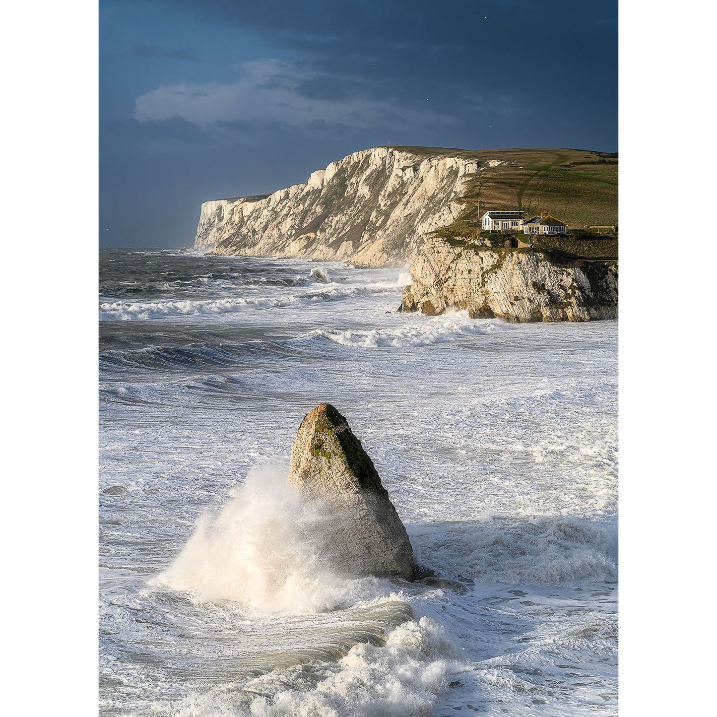 Majestic cliffs and rugged rocks dominate the scene in "Freshwater Bay" by Available Light Photography. A quaint house perches near the cliff's edge under a brooding sky, capturing nature’s raw power and beauty.