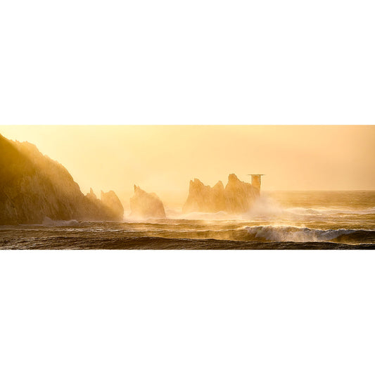 Waves crash majestically against the rocky coastline in "The Needles" by Available Light Photography. Bathed in golden sunlight, a small structure stands visible in the distance—a serene yet captivating seascape for your senses.