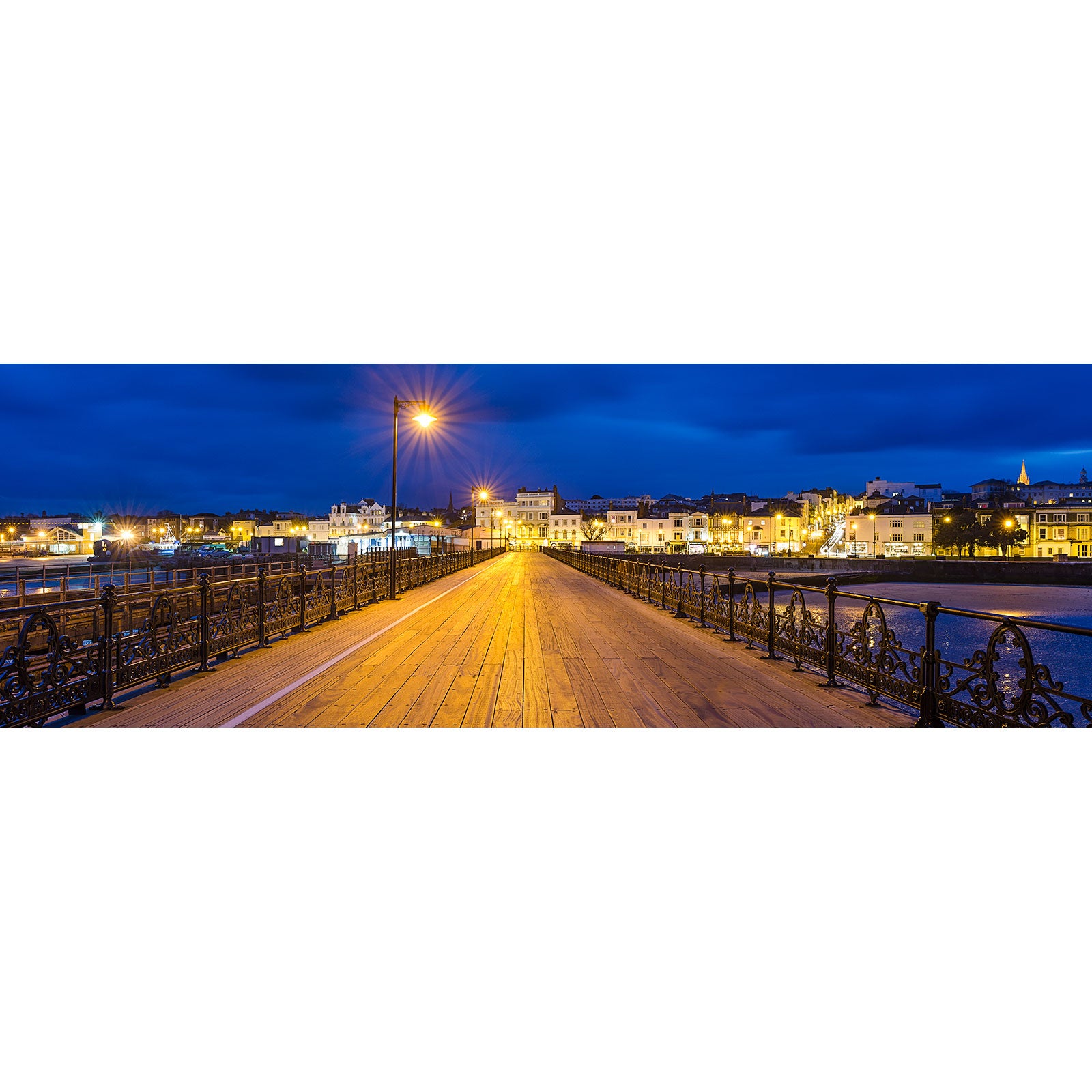 A Ryde wooden pier illuminated by street lamps at dusk with the Isle skyline in the background captured by Available Light Photography.