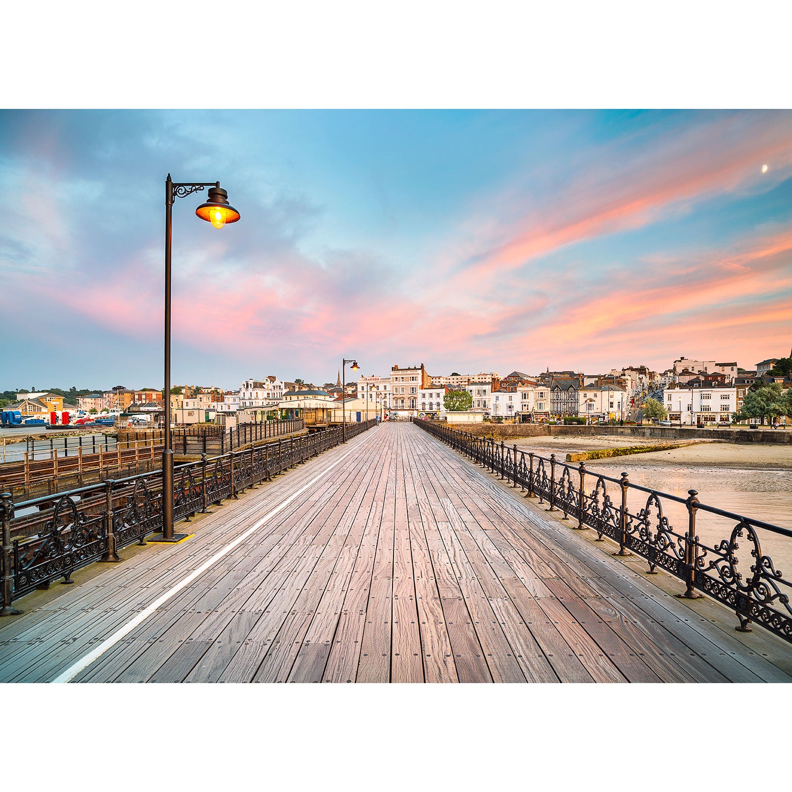 A Ryde Pier leading towards the Isle of Wight coastal town during a colorful sunset with street lamps and iron railings, captured by Available Light Photography.