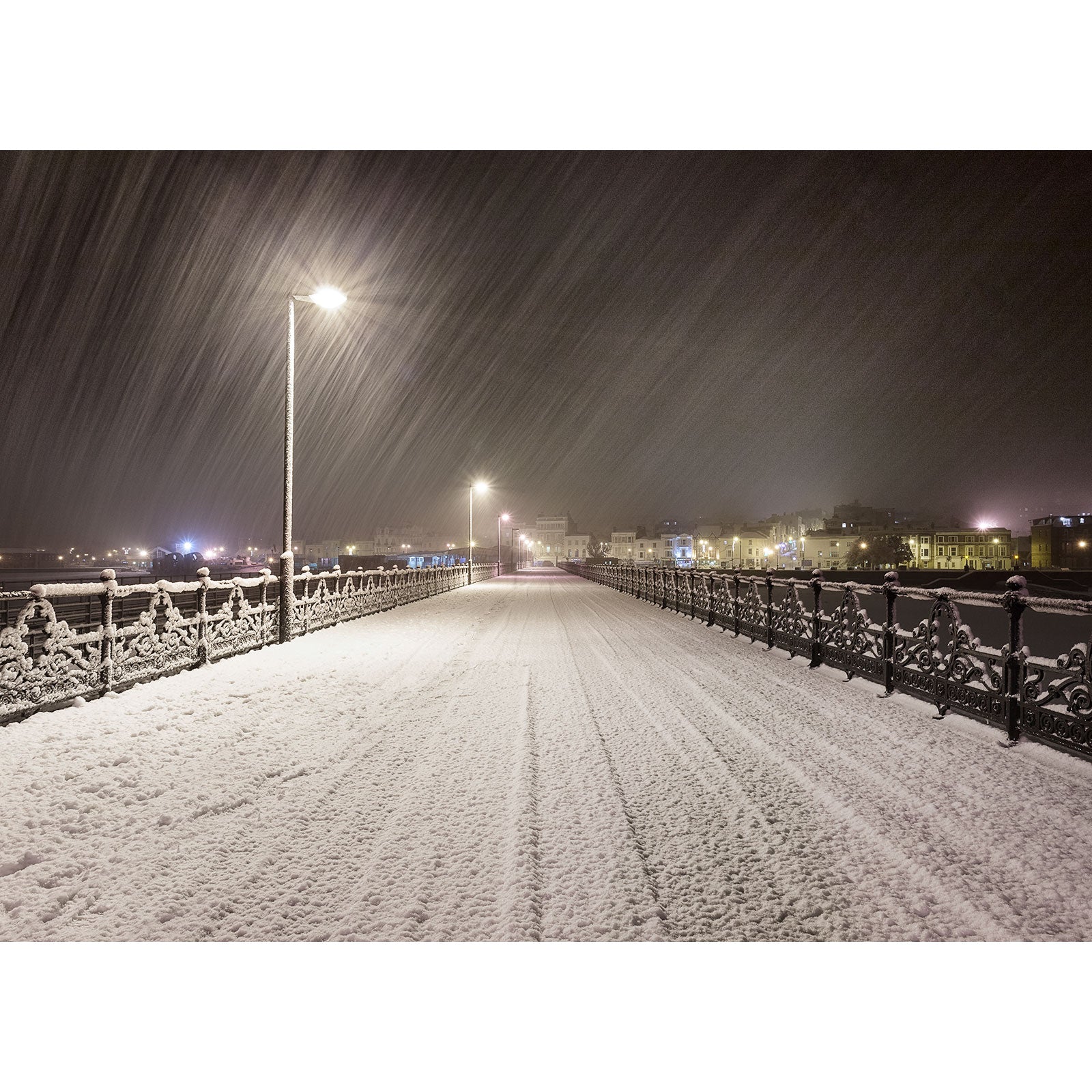 A snow-covered Ryde Pier in the snow at night, illuminated by streetlights with snowflakes falling on the Isle of Wight by Available Light Photography.