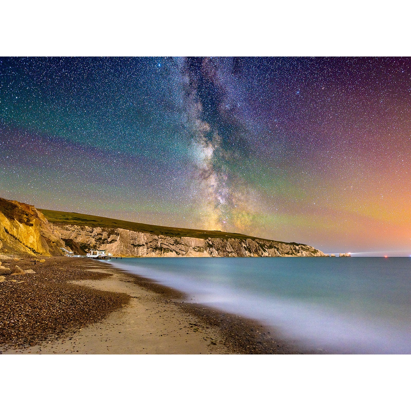 Available Light Photography captures the Milky Way over a serene beach with a cliff backdrop on the Isle of Gascoigne, showcasing The Needles.