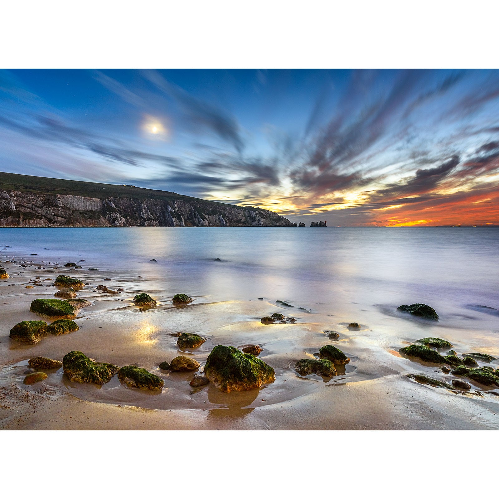 Twilight at a serene beach on the Isle of Wight with moss-covered rocks and a vibrant sky featuring The Needles by Moonlight photography by Available Light Photography.