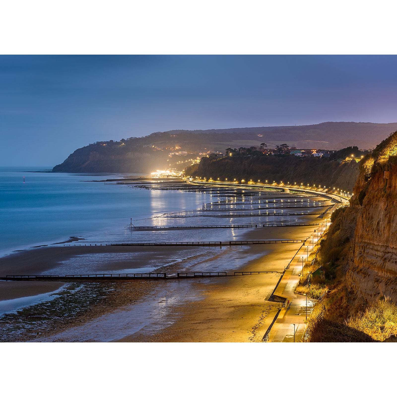 Illuminated coastline with a serpentine promenade at twilight, reminiscent of Lake Beach looking towards Shanklin by Available Light Photography.