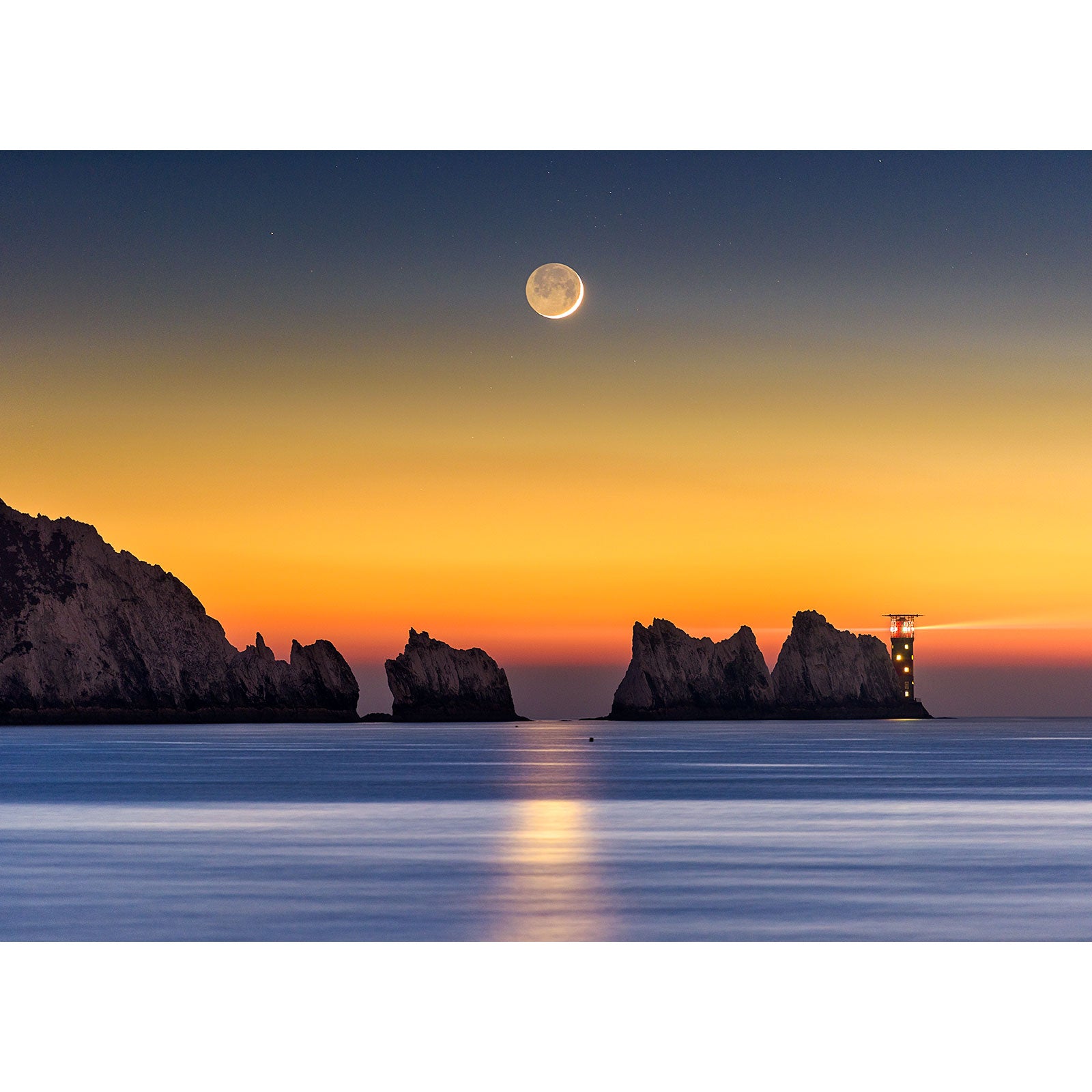 A serene seascape at twilight with a Crescent Moon above rocky cliffs on the Isle of Wight captured by Available Light Photography's Crescent Moon - The Needles.