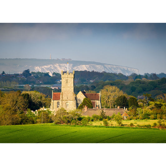 A rural landscape on the Isle of Wight with Godshill Church in the foreground and chalk cliffs in the distance under a hazy sky, captured by Available Light Photography.