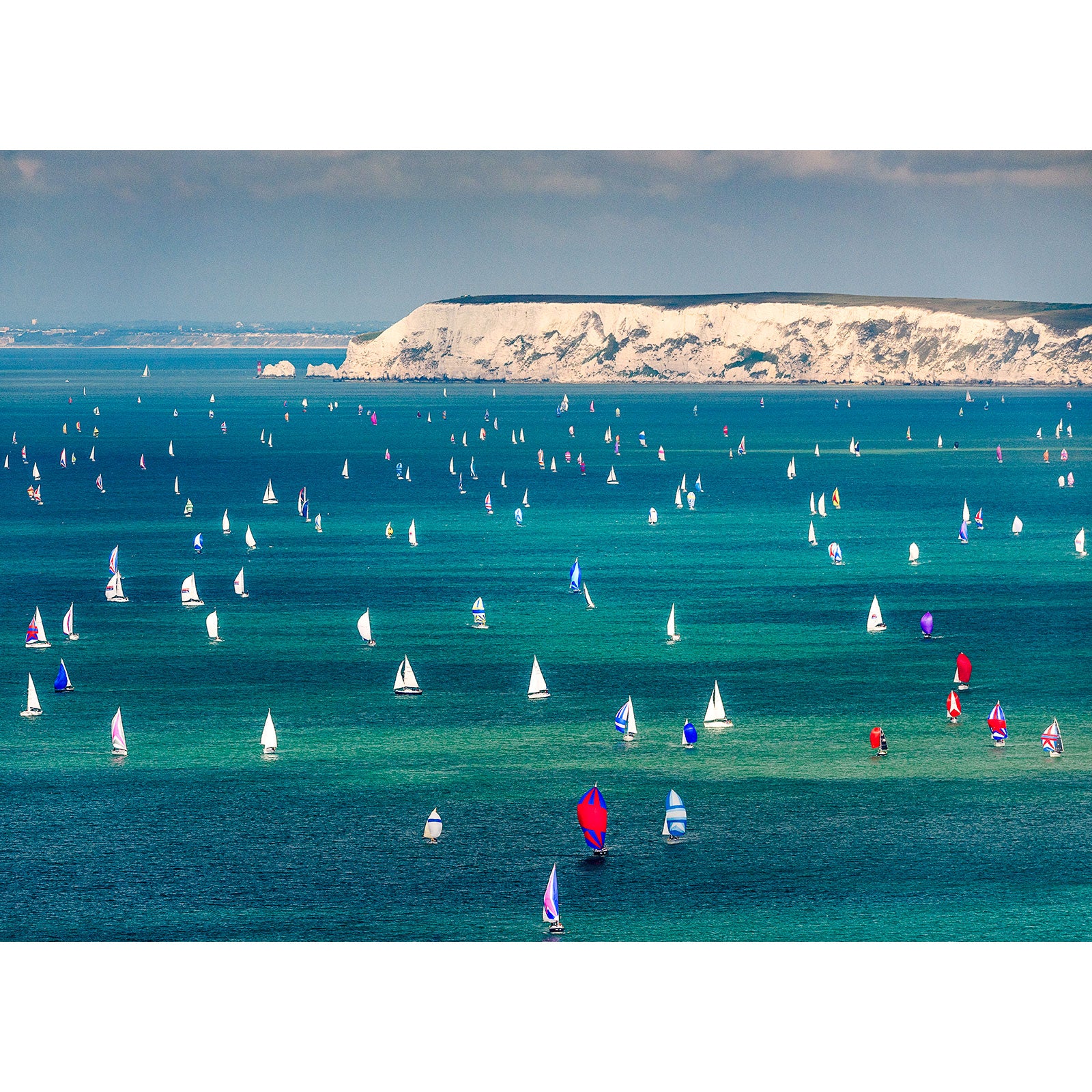 Sailboats participating in the Round the Island Race regatta on a bright day with the white cliffs of Wight in the background. (Brand name: Available Light Photography)