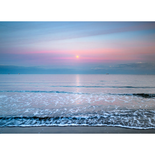 Tranquil sunset over a calm ocean with gentle waves lapping the shore of Sandown Bay.