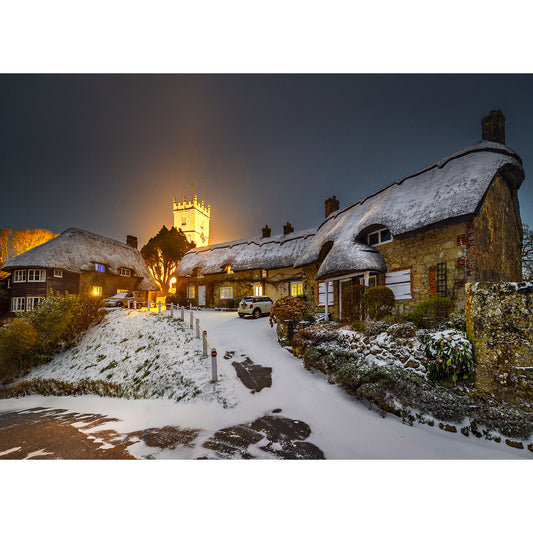 A tranquil evening on the Isle of Wight with snow-covered thatched-roof cottages and Godshill Church illuminated in the backdrop, captured beautifully by Available Light Photography.