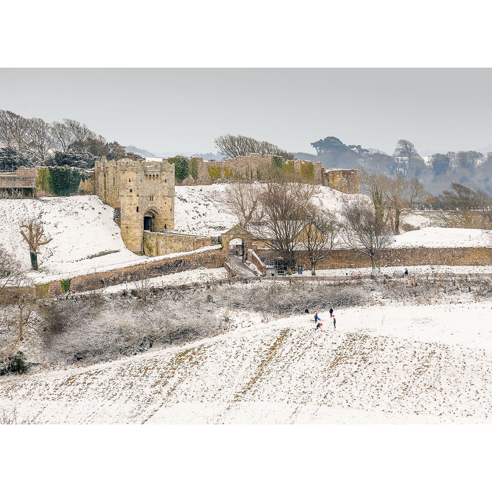 Snow-covered landscape with people walking near Carisbrooke Castle on a cloudy day captured by Available Light Photography.