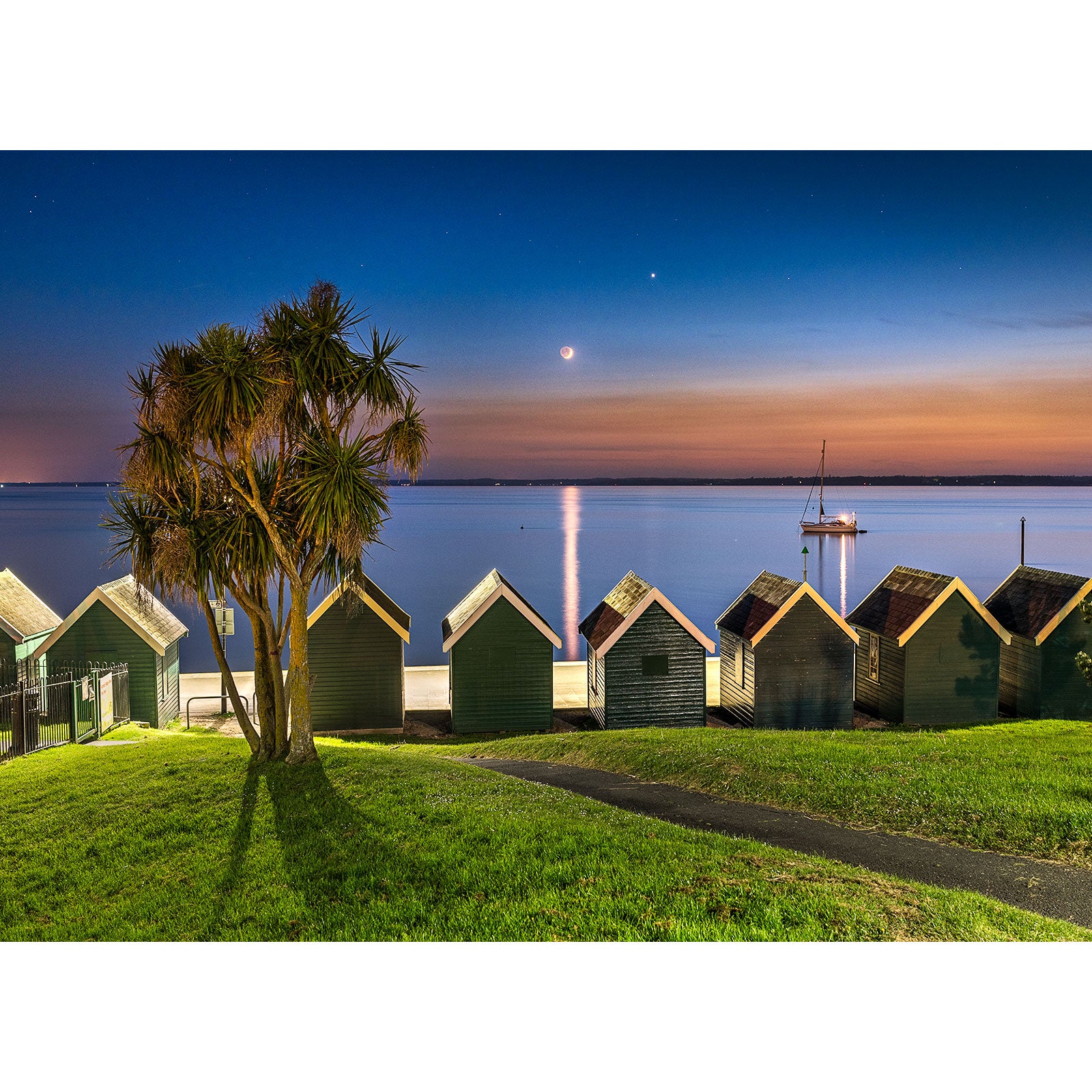 Beach huts by the sea at twilight on the Isle with a clear view of the Crescent Moon by Available Light Photography.