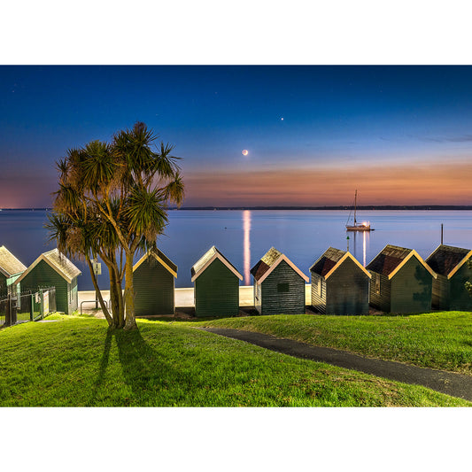 Beach huts by the sea at twilight on the Isle with a clear view of the Crescent Moon by Available Light Photography.