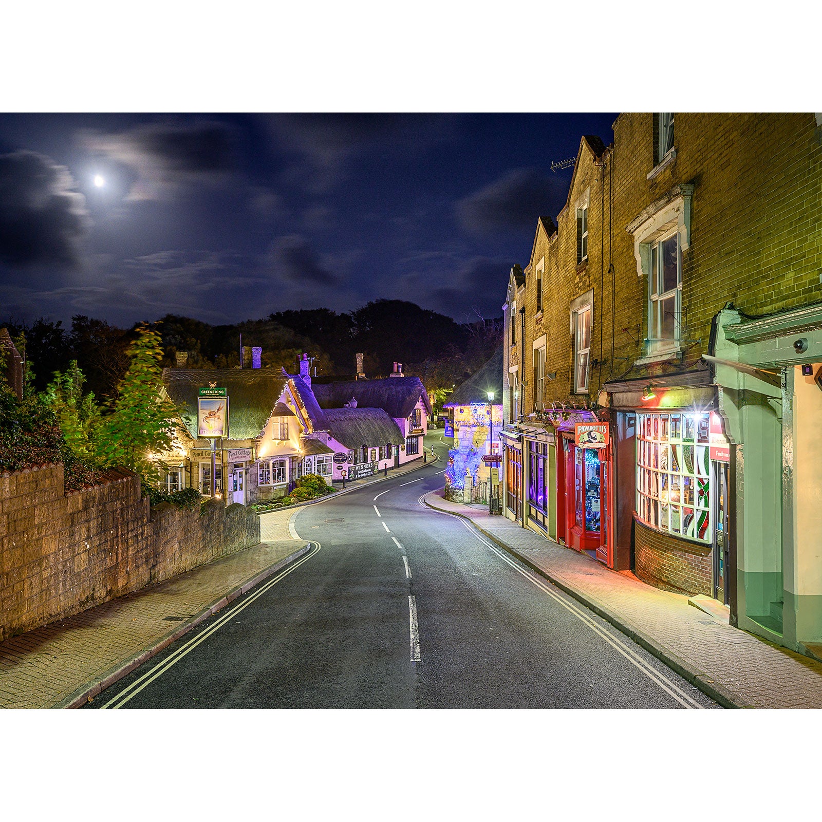 A tranquil nighttime view of Shanklin Old Village in a quaint Isle with vintage buildings and a glowing full moon captured by Available Light Photography.