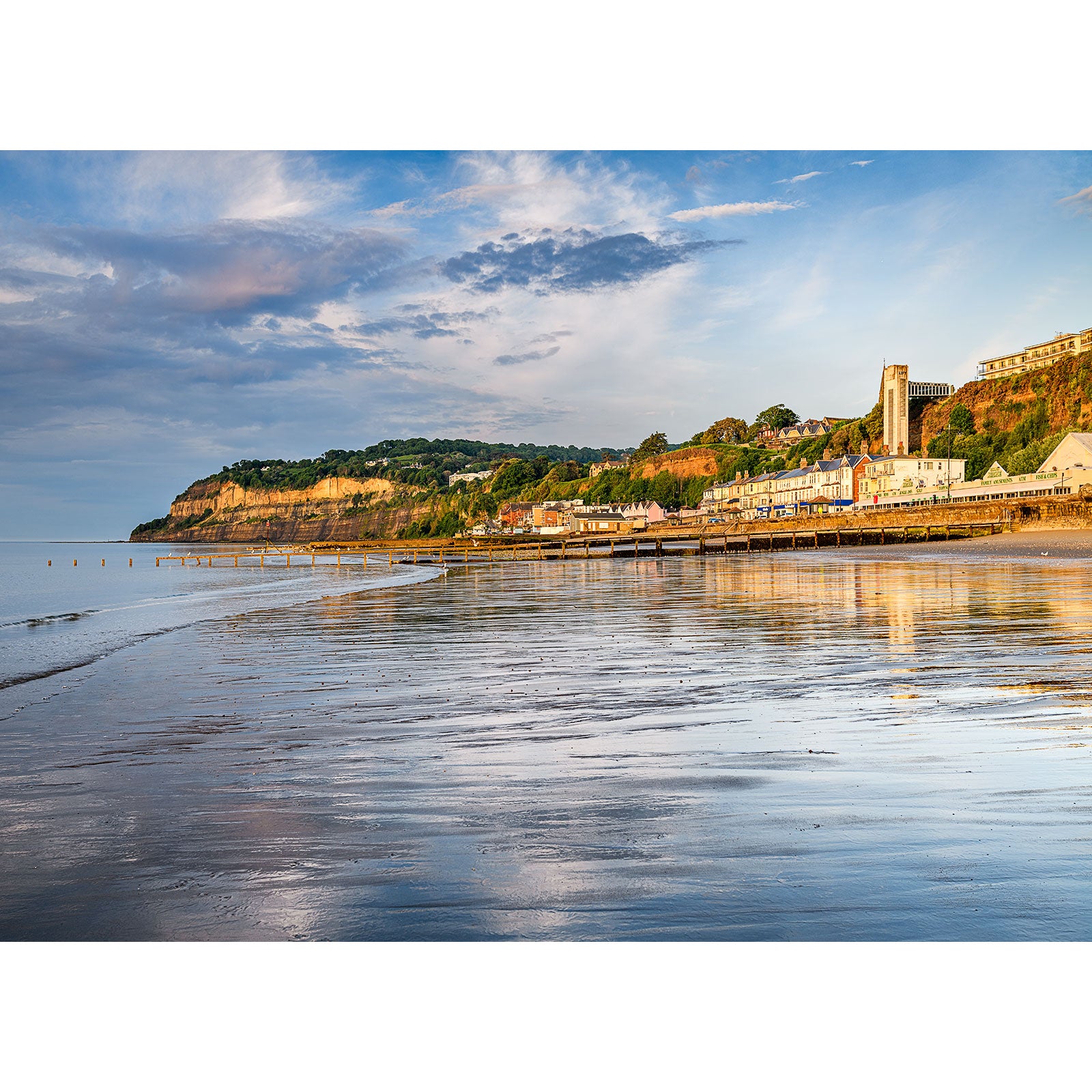 Coastal town at low tide with reflective wet sand, cliffs, and buildings under a blue sky on the Isle of Wight by Available Light Photography's Shanklin.