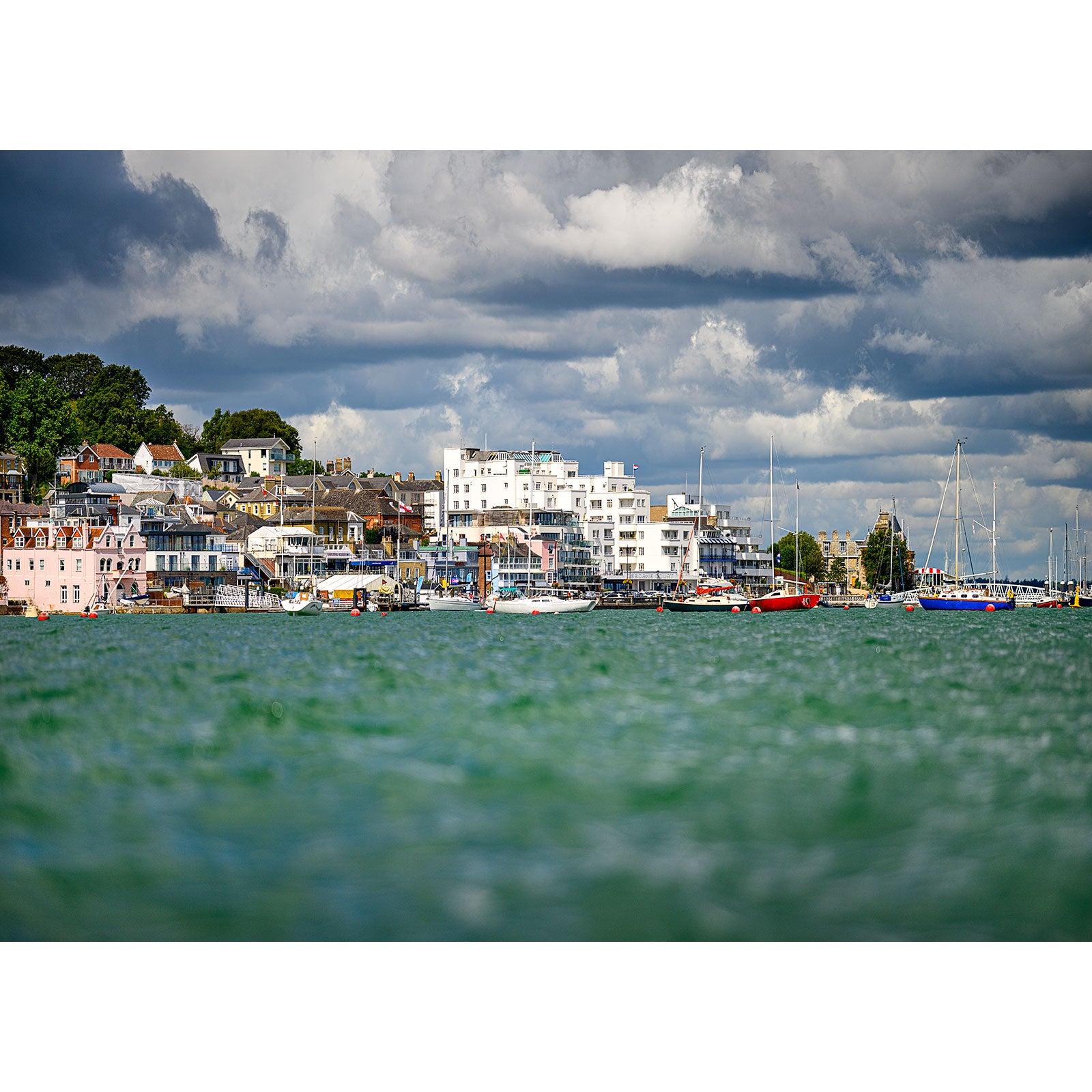 Coastal town on the Isle of Wight with modern buildings and moored boats under a dramatic cloudy sky, captured by Available Light Photography's Cowes.