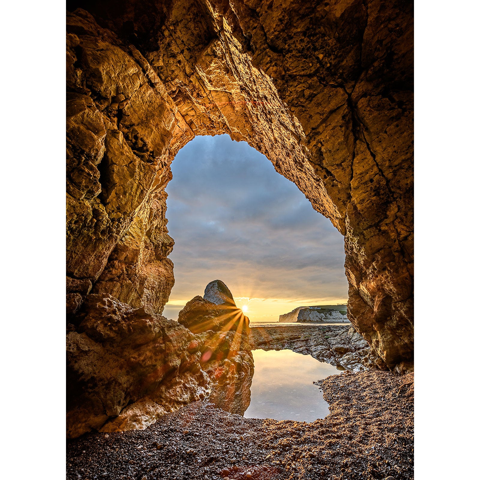 Sunset viewed through a natural archway on the Isle of Wight's rocky shore in the In the Caves, Freshwater Bay photograph by Available Light Photography.