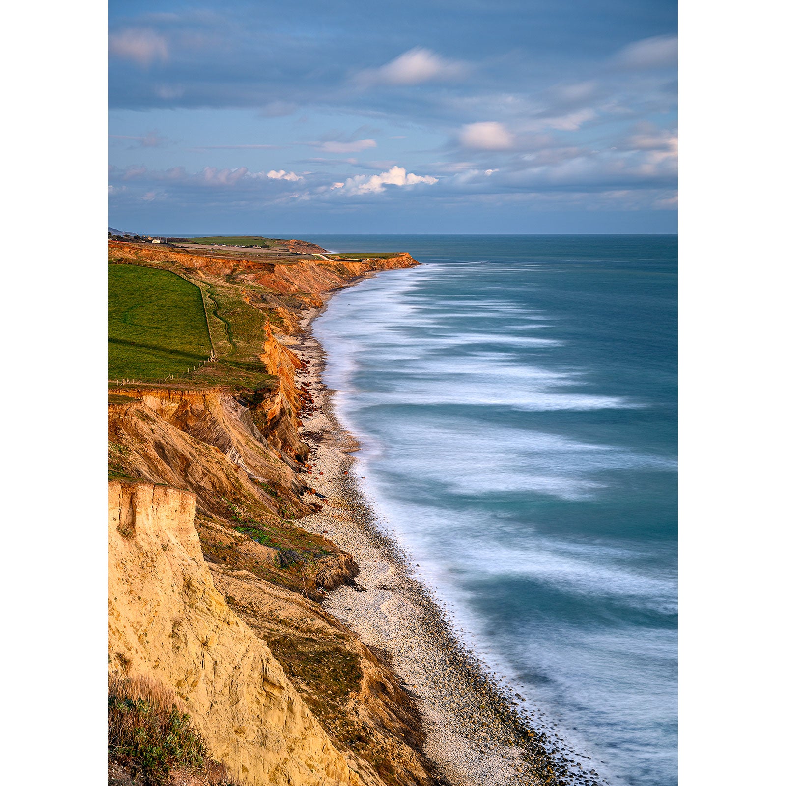 Cliff-lined coast with a pebbly shore and rolling waves under a partly cloudy sky on Compton Bay by Available Light Photography on the Isle of Wight.