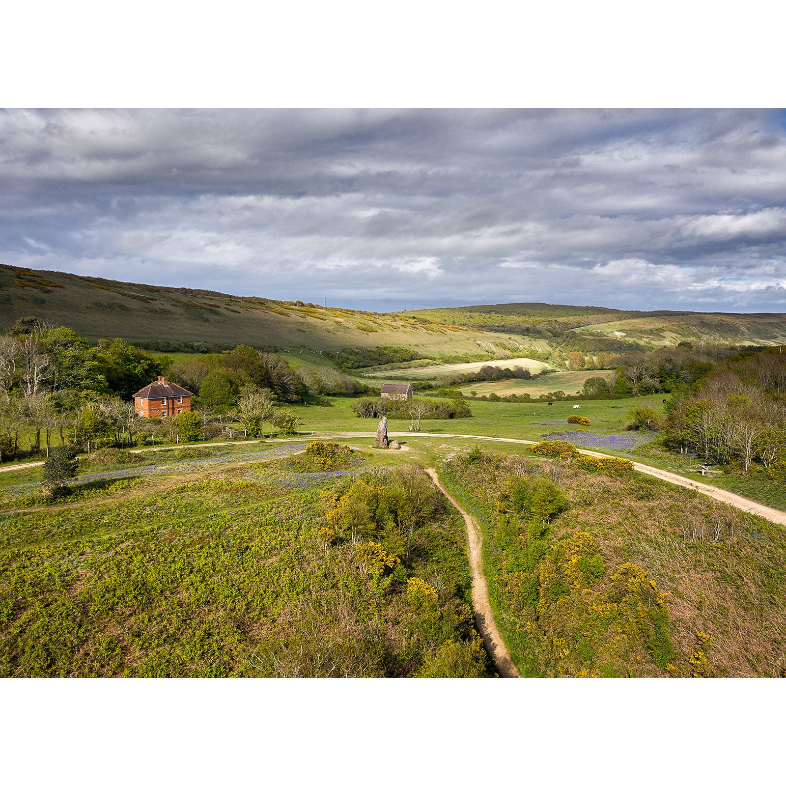 Pastoral landscape with a winding path leading to a Longstone house amidst lush greenery under a cloudy sky captured by Available Light Photography.